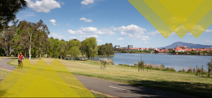 A cyclist riding past Lake Tuggeranong, the tuggeranong town centre is seen across the lake